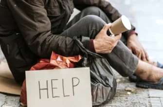 A homeless man sitting outdoors with a cardboard help sign